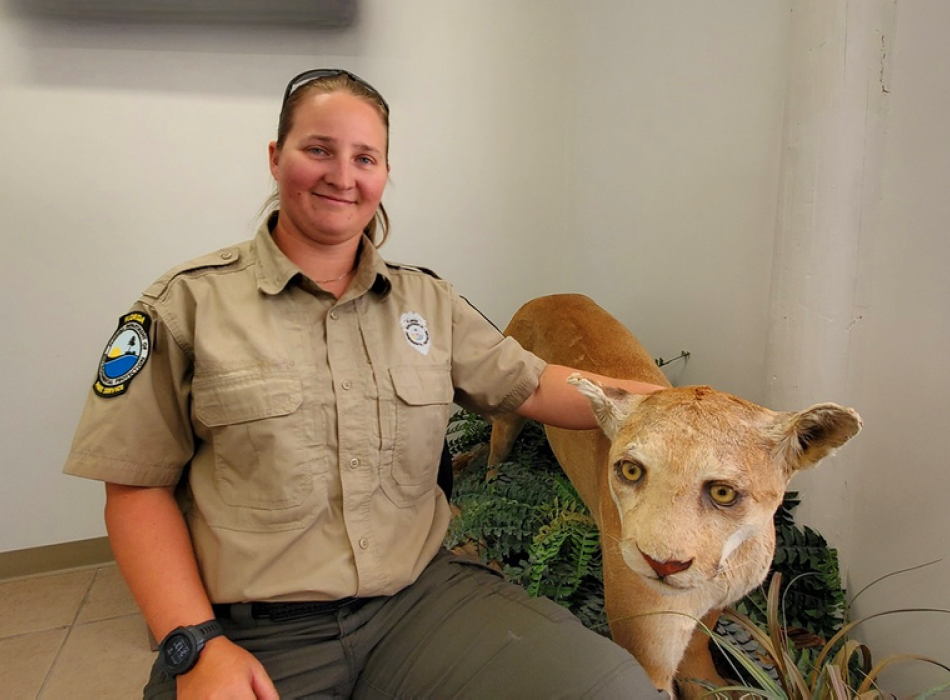 Person seated wearing tan shirt and green pants. Florida panther