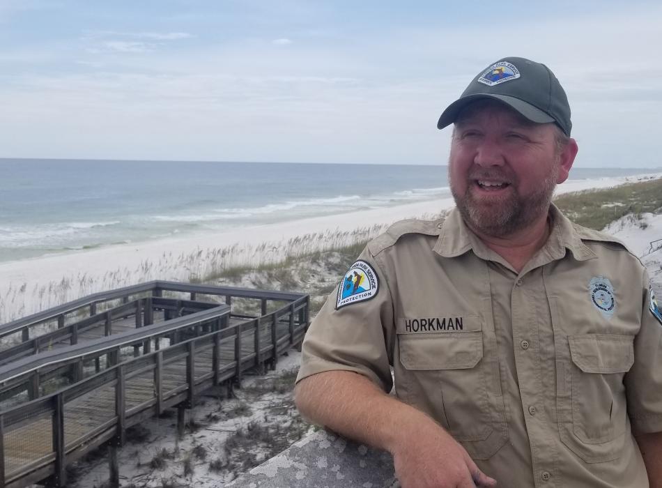 Chris, a Florida park service ranger standing on a boardwalk, overlooking the ocean.