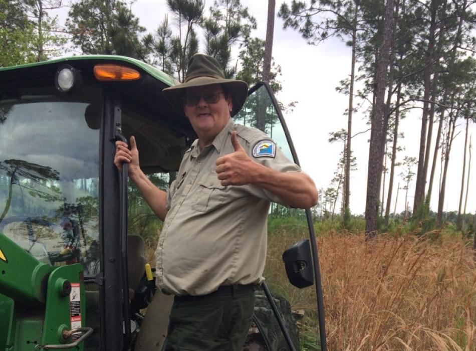 a man in uniform gives a thumbs-up while hanging onto a large tractor