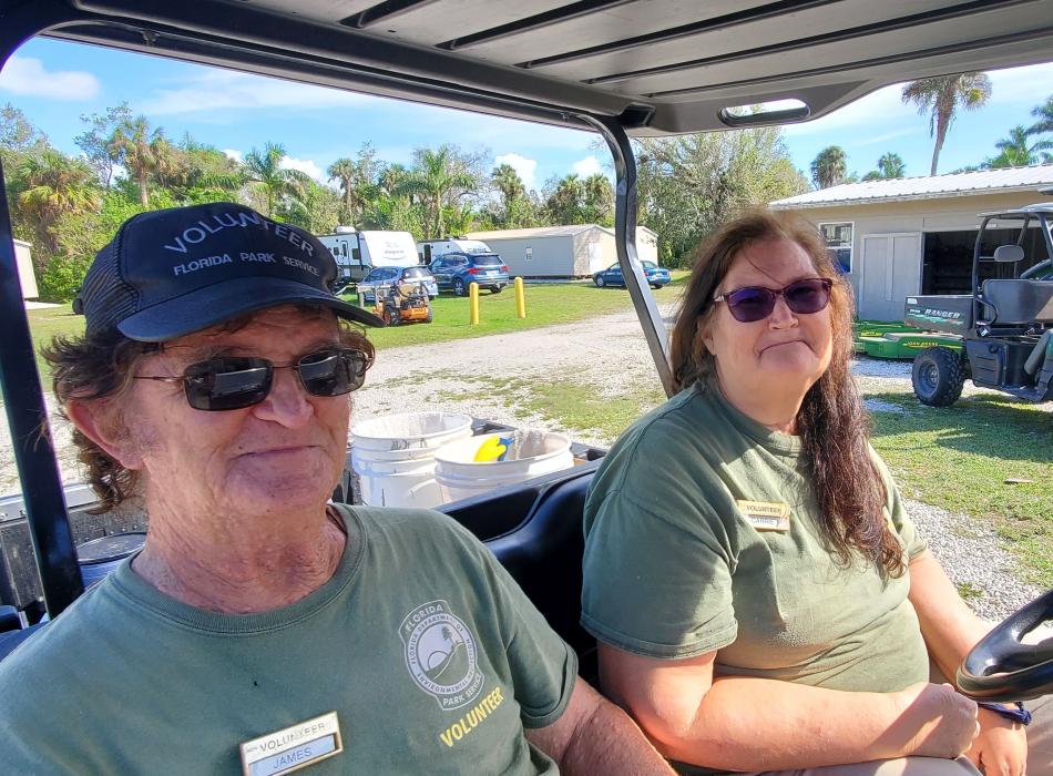 Two persons in a golf cart wearing green shirts