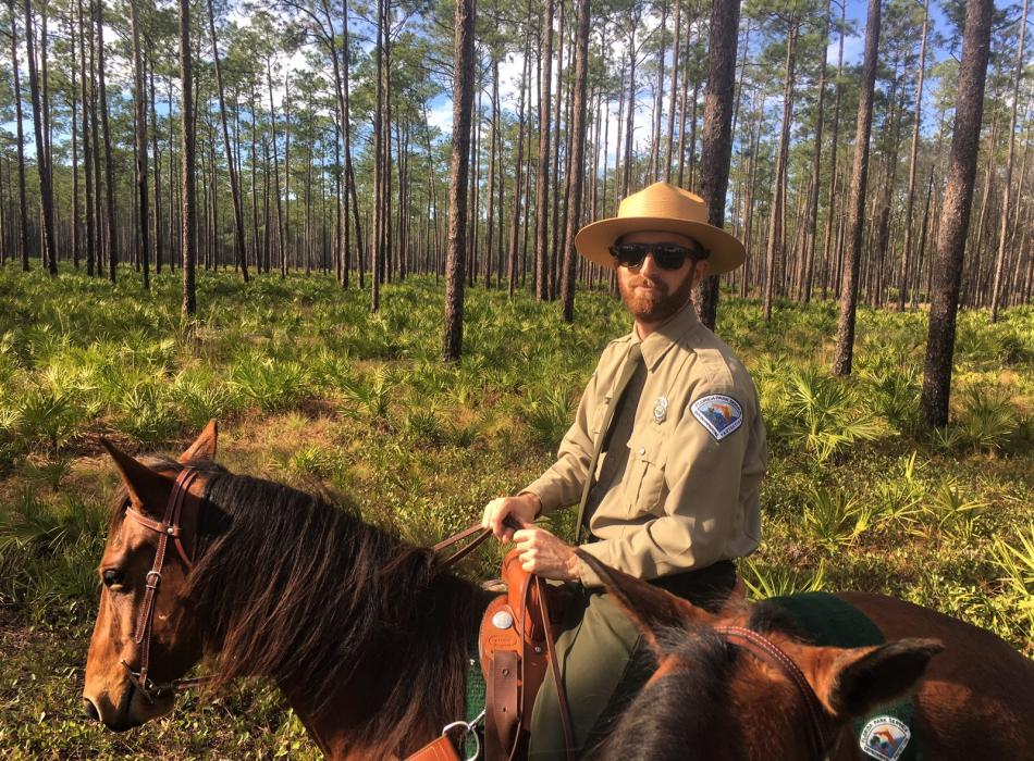 Jesse, on a horse in a clearing, smiling at the camera.