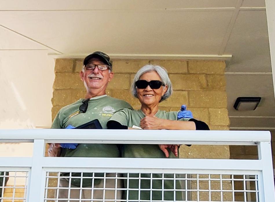 Two people wearing green shirts. One wearing sunglasses. 