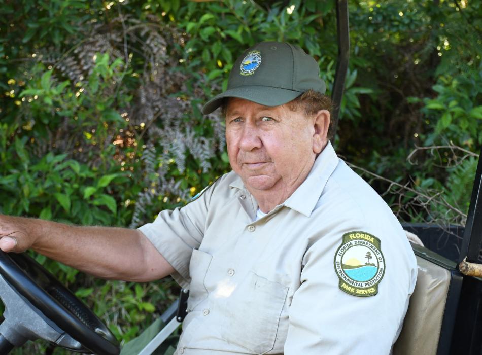 Man driving cart wearing green hat and tan shirt