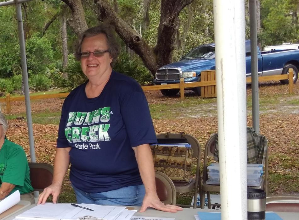 A woman in a blue shirt stands under a tent smiling. 