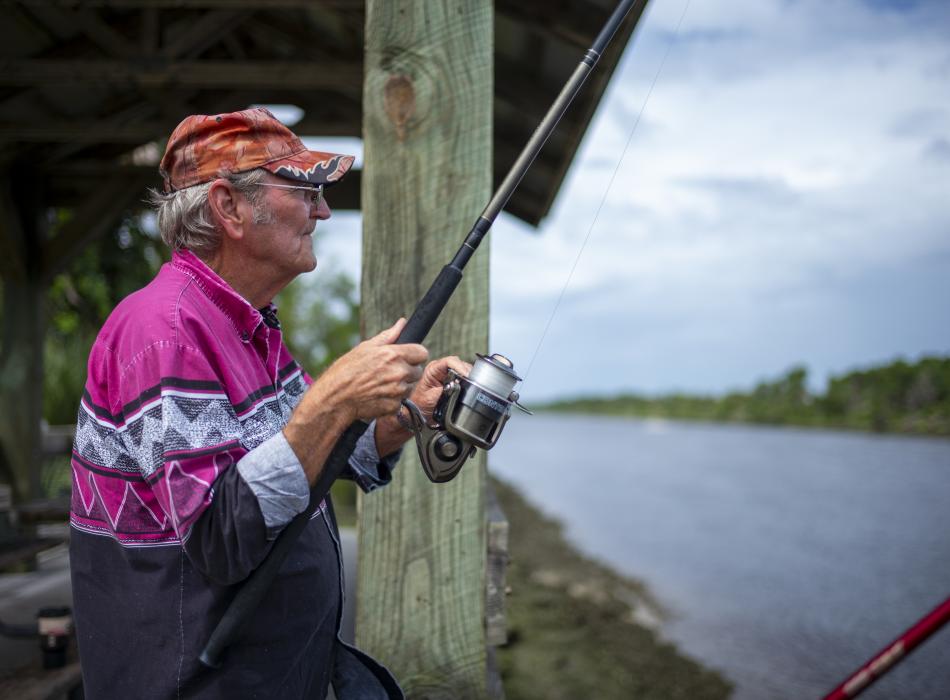 An elderly man fishing, looking out over the water. 
