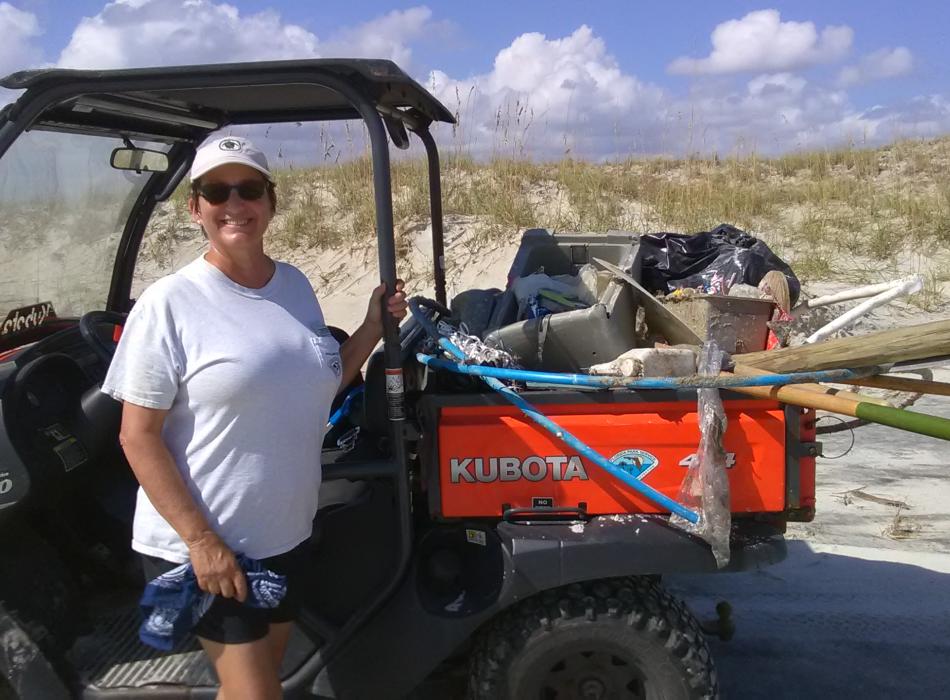 Volunteer Linda standing by an ATV on the beach smiling at the camera 