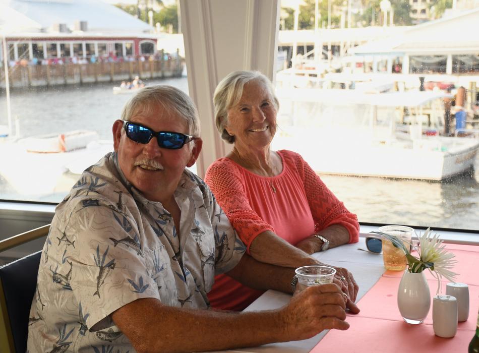 Man wearing sunglasses, woman wearing pink shirt sitting at a table on a boat