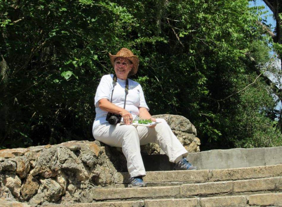 A woman in a hat with a camera around her neck sits on stone stairs.