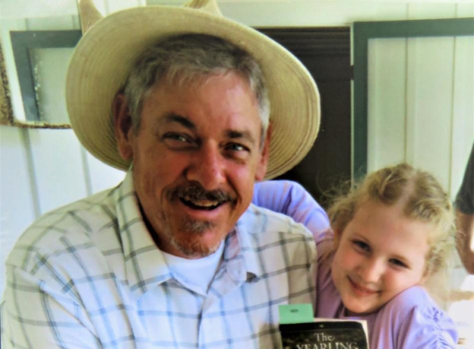 a man in period dress hugs a small girl with a copy of the book the yearling