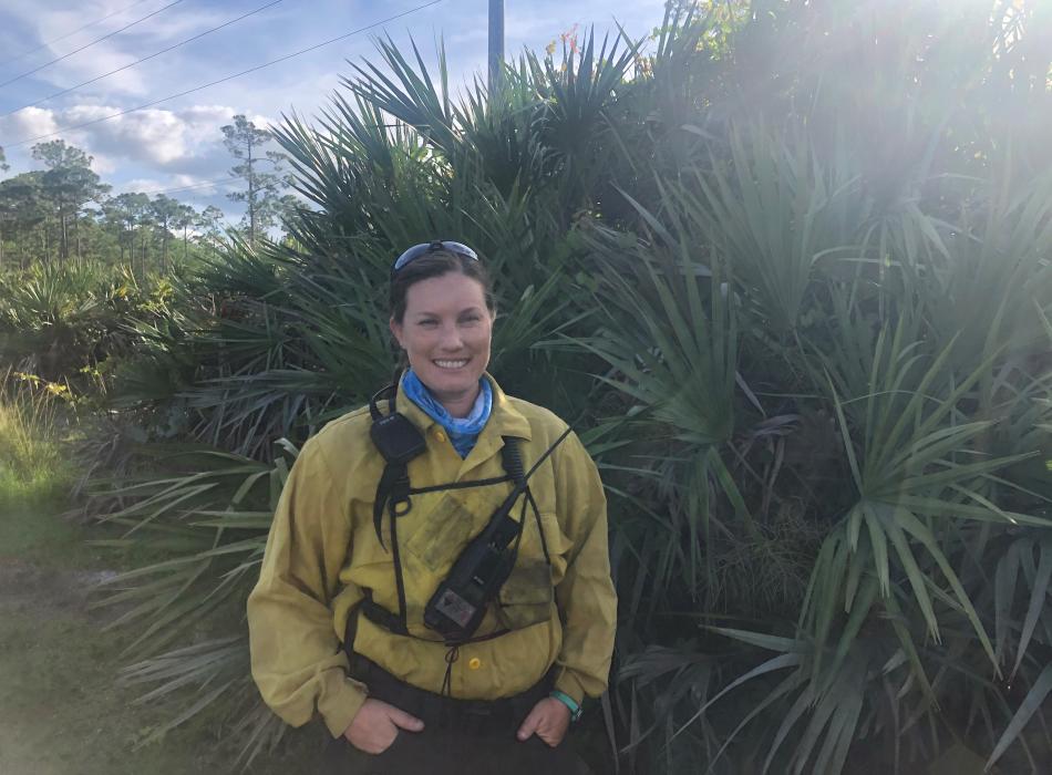 Park Ranger Sara Travis stands with native vegetation in fire gear before a burn