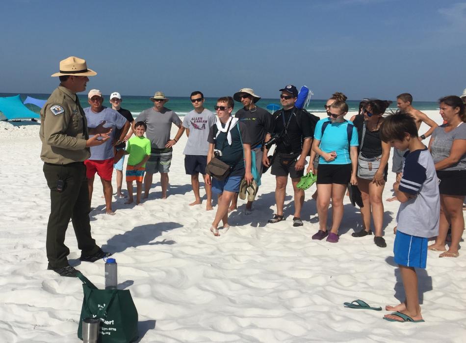 Park Ranger speaks to large group of people on the white sandy beach.