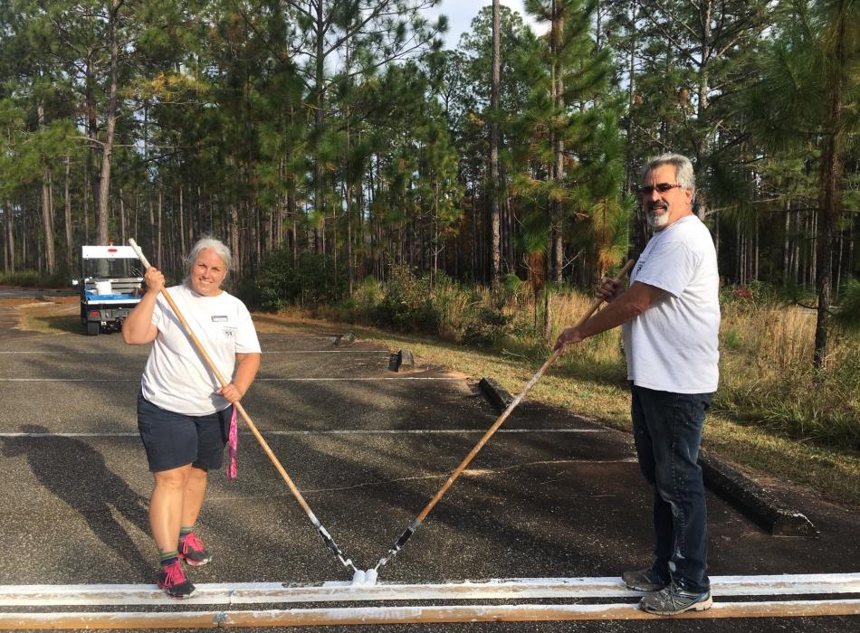 Man and woman hold paint rollers painting parking lot lines. 