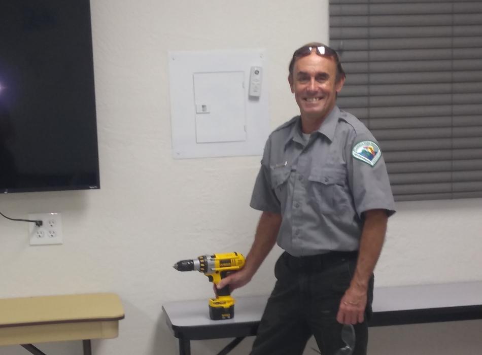 Gary, holding a drill and smiling at the camera.