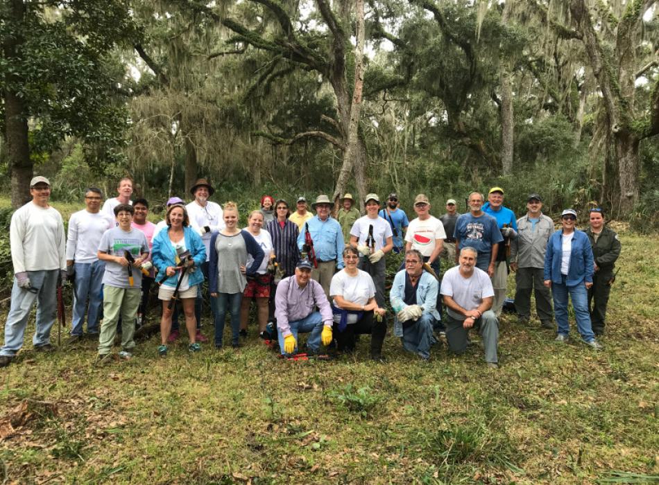 a large group of people in work clothes stands underneath a canopy of trees