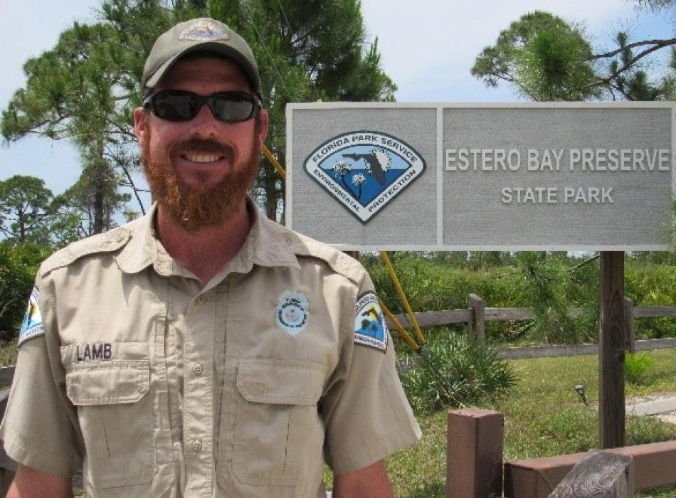 Justin Lamb standing in front of the park entrance sign, smiling at the camera..