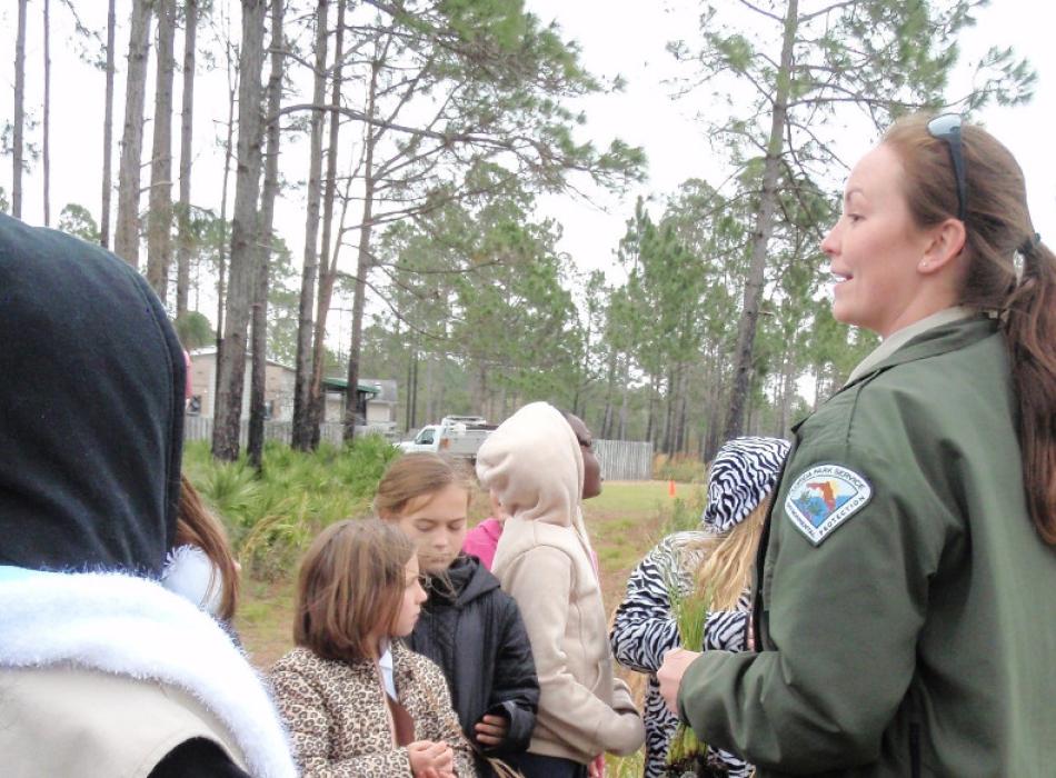 a woman in uniform talks to a group of children outside