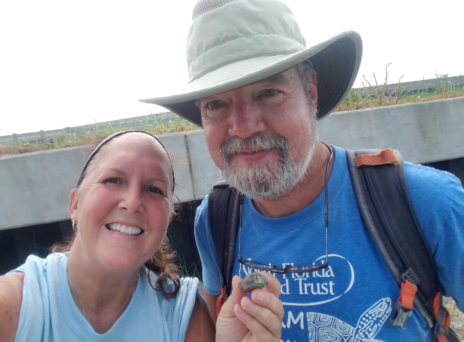 a man and woman in field clothes smile at the camera while holding some sort of small artifact