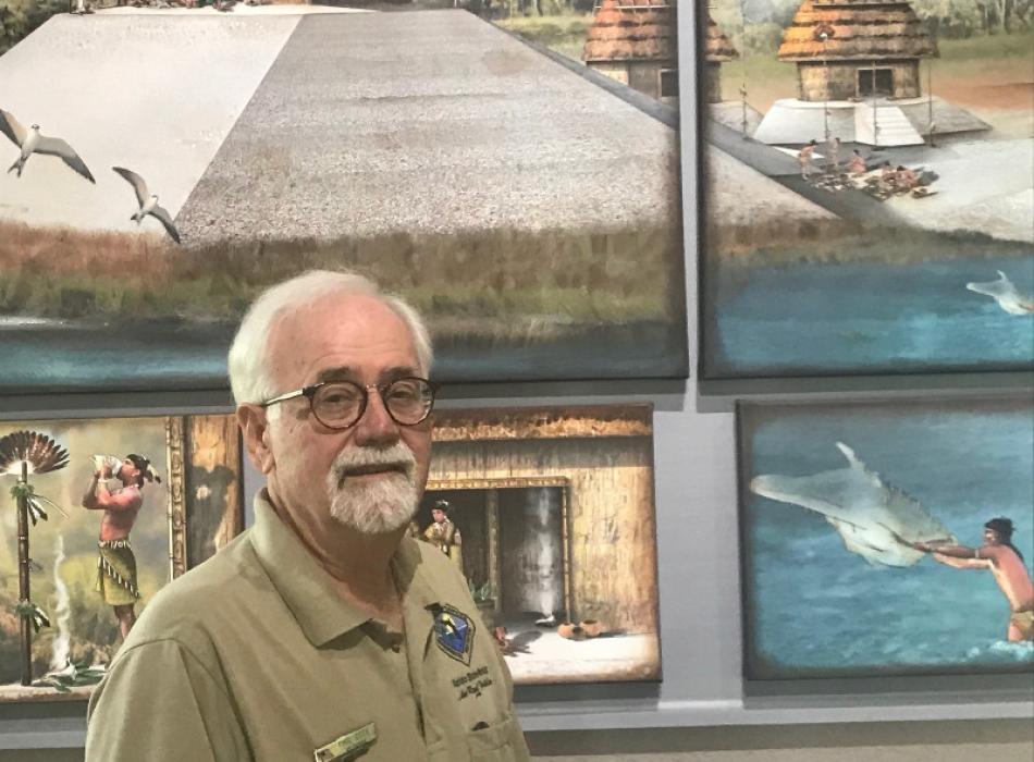 a man stands in front of a backdrop depicting a native american site.