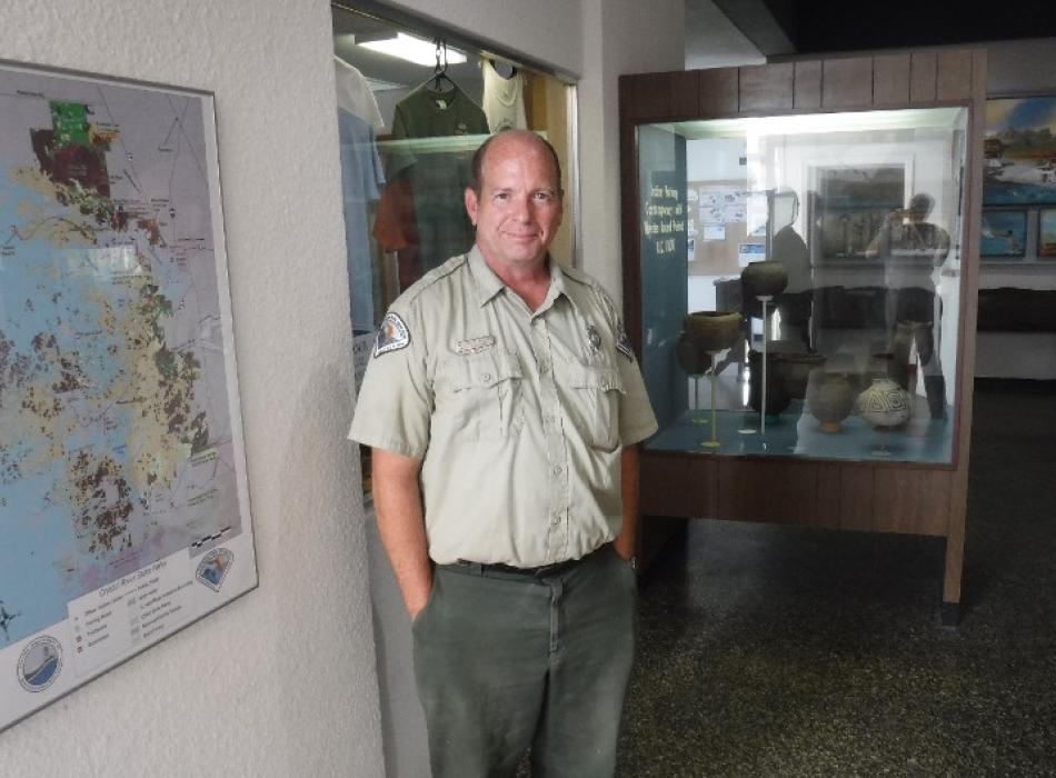 a man stands with his hands in his pockets in a museum wearing a park ranger uniform.