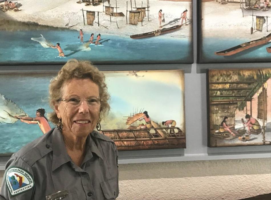 A woman in volunteer uniform stands in front of a museum background