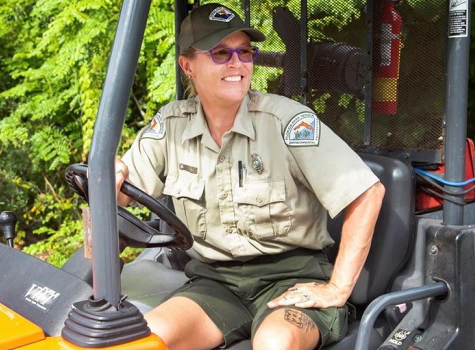 Shara Marconi dressed in her park ranger uniform sitting on a park UTV , smiling off into the distance