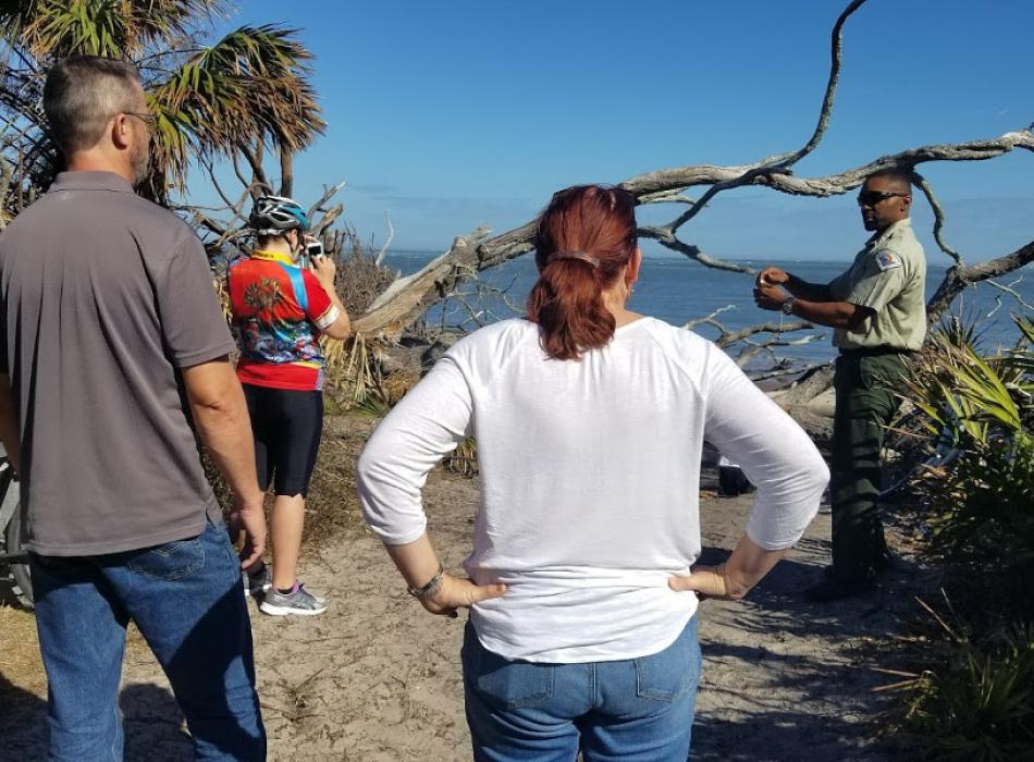 a park ranger points at a beach habitat for several visitors.