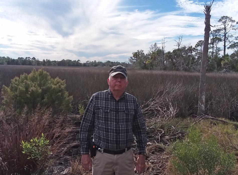 A man stands in front of a scrub habitat