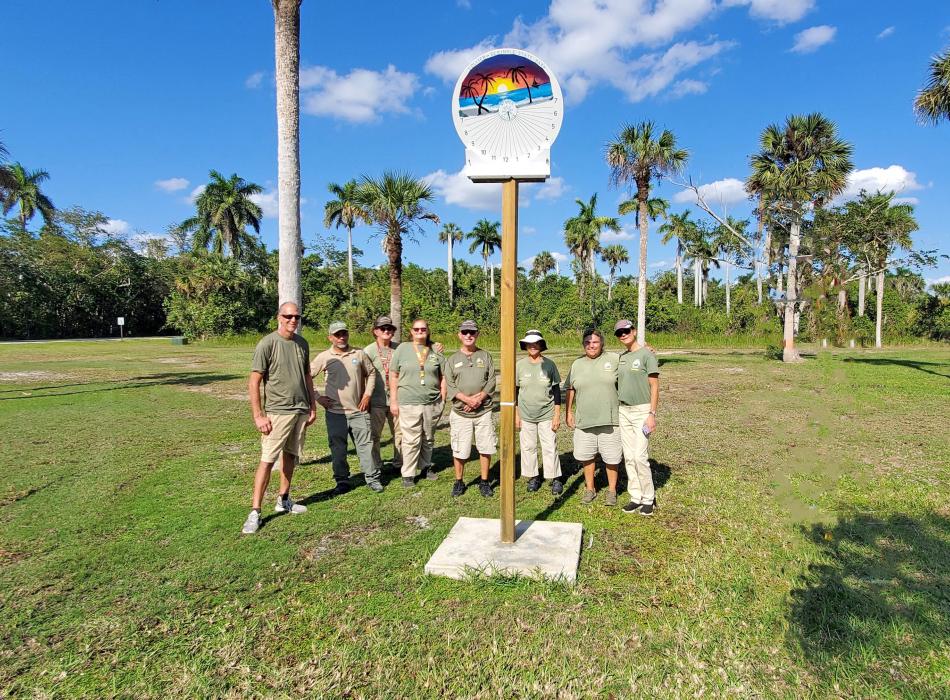 Park volunteers standing next to a sundial with palms, green grass and blue sky