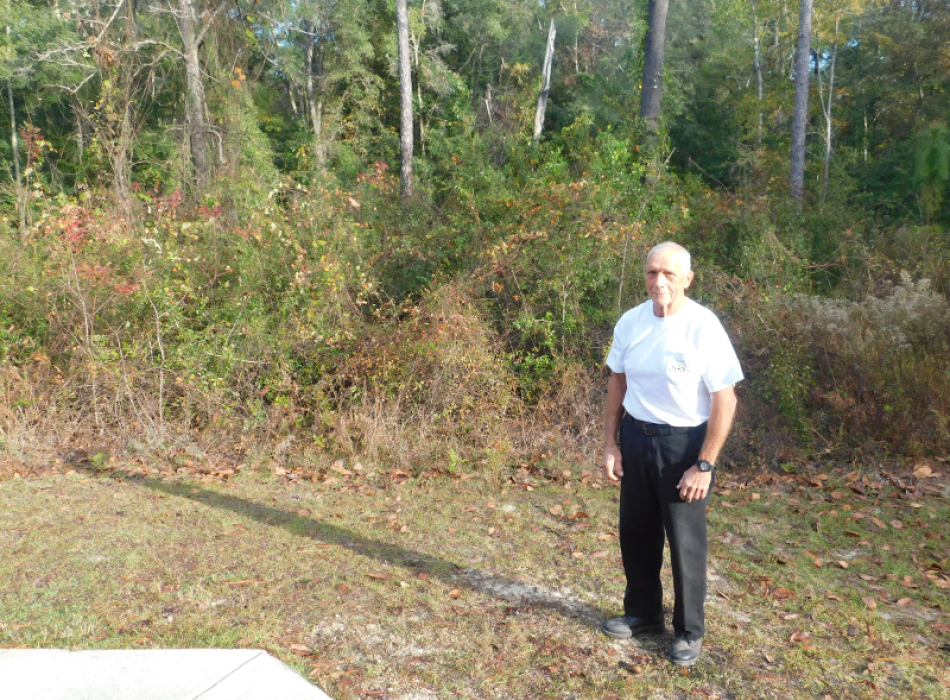 Volunteer Bill Cade stands beside as park trail, with hammock trees in the background.